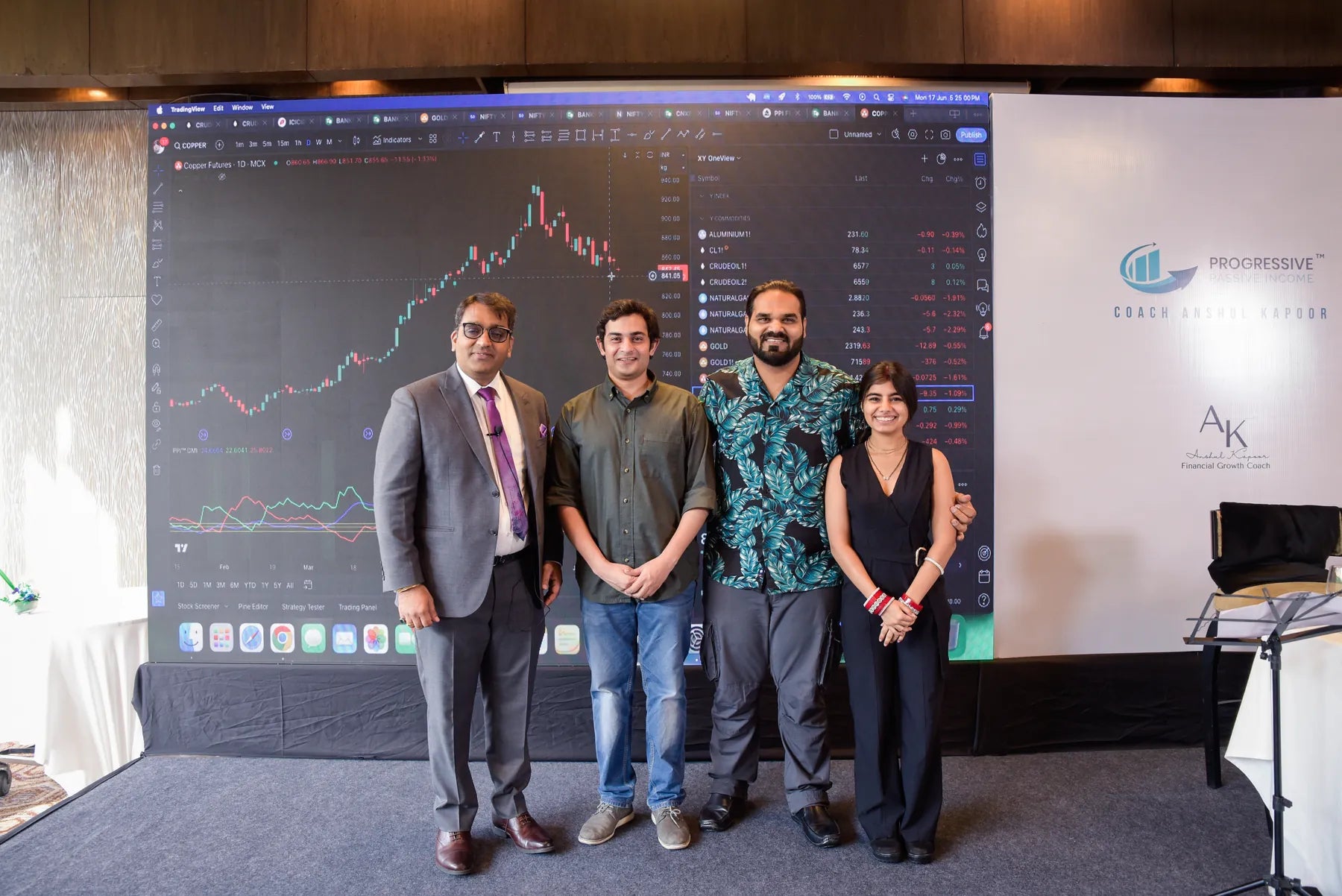 Anshul Kapoor standing with three other people in front of a large screen showing a market chart at a programme event