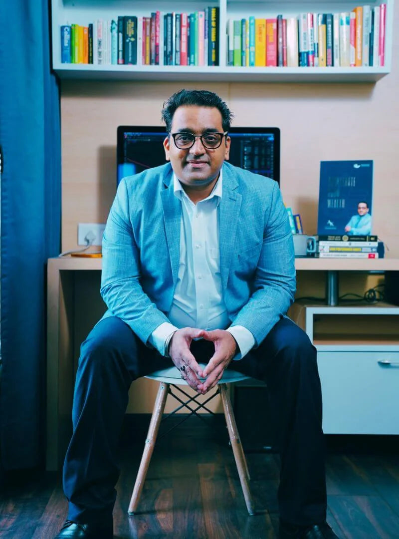 Anshul Kapoor seated in his office in a light blue blazer, with a bookshelf and a monitor behind him