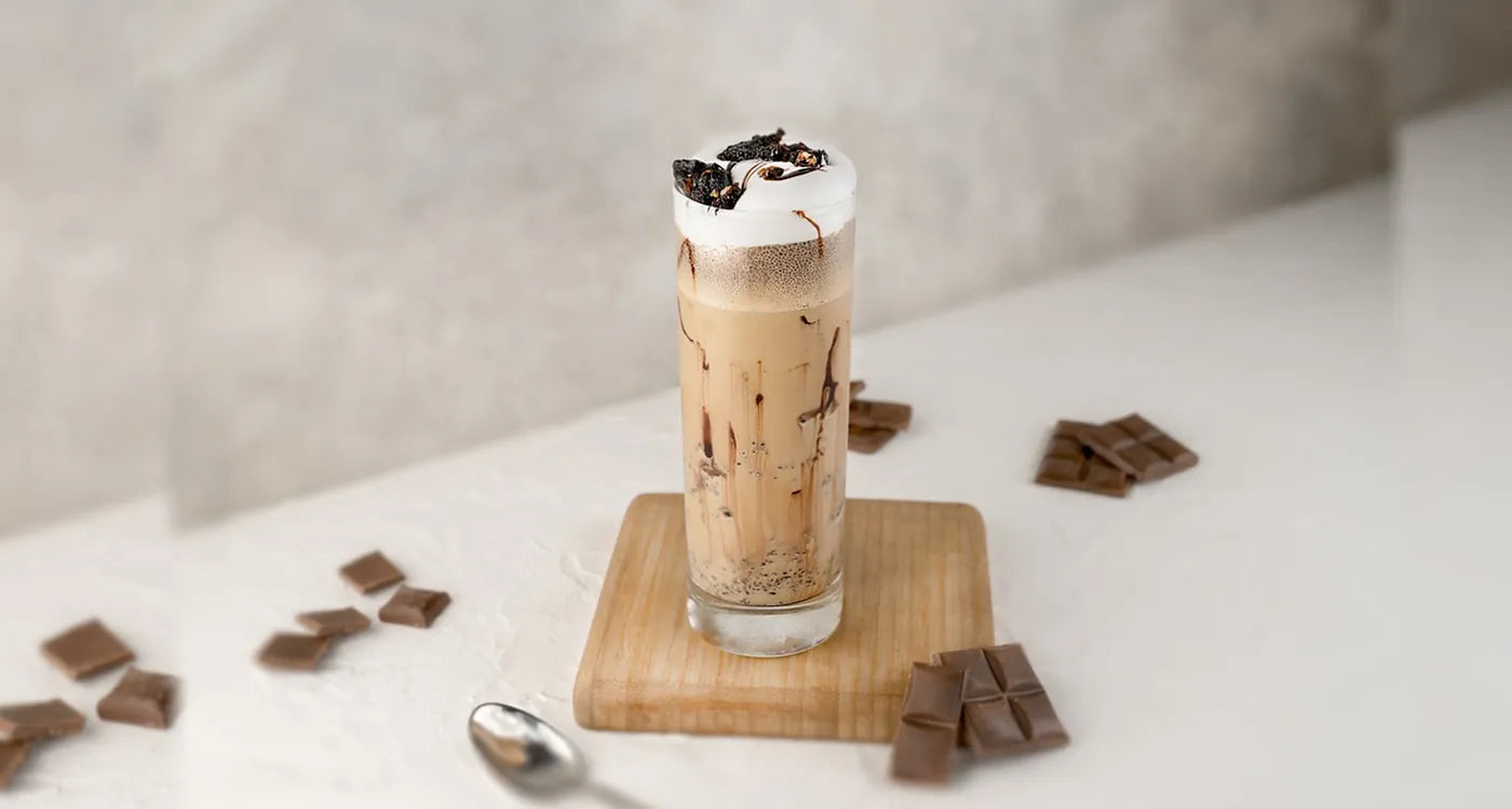 An iced chocolate coffee topped with cream and cookie crumbs, with chocolate pieces scattered around
